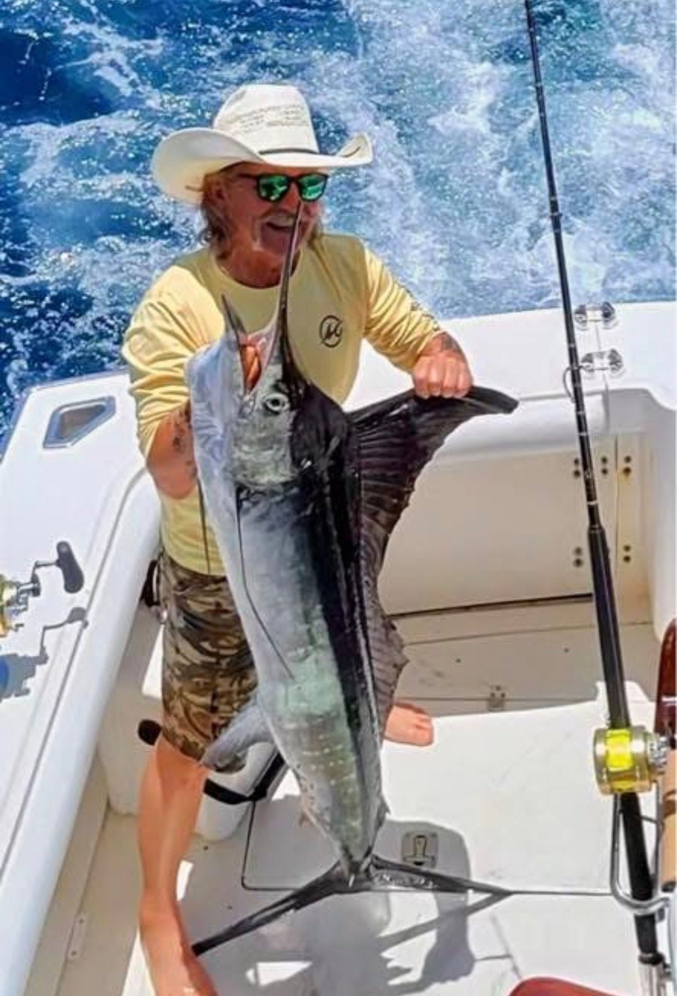 Angler on a boat holds a large fish against a sunny blue ocean background