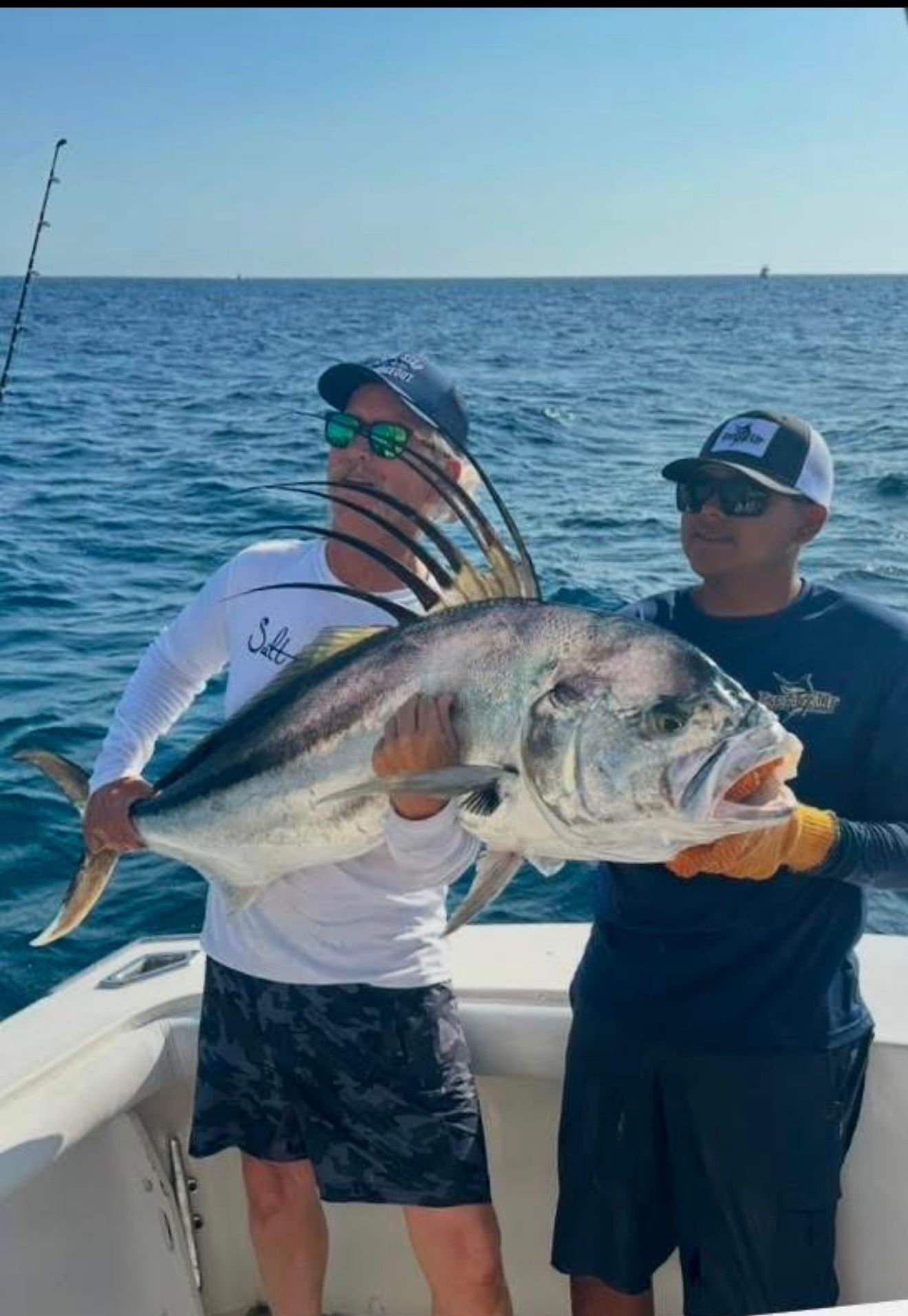 a man and a woman are standing on a boat holding a large dorado fish .