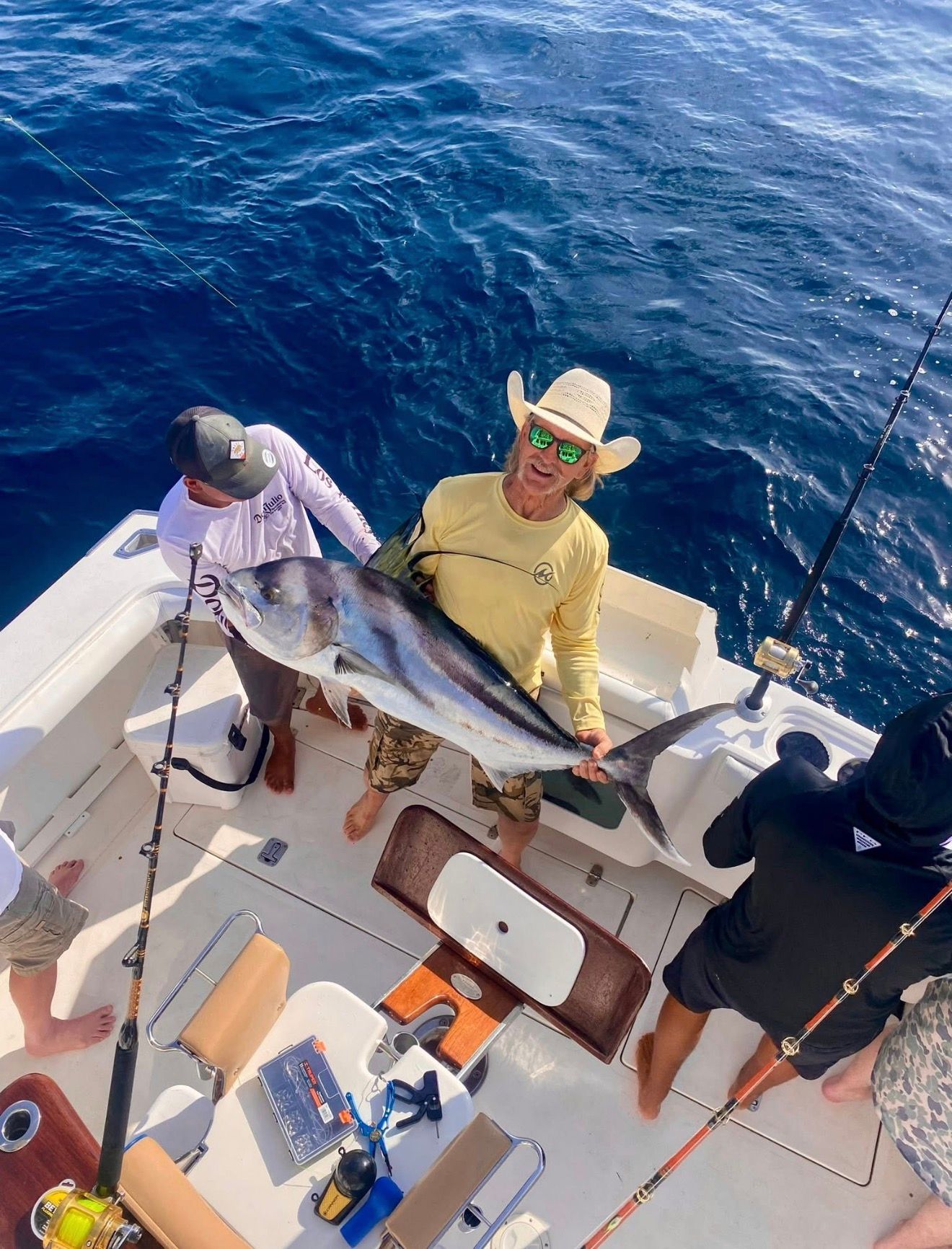 Two anglers on a boat hold a large fish over deep blue ocean water.