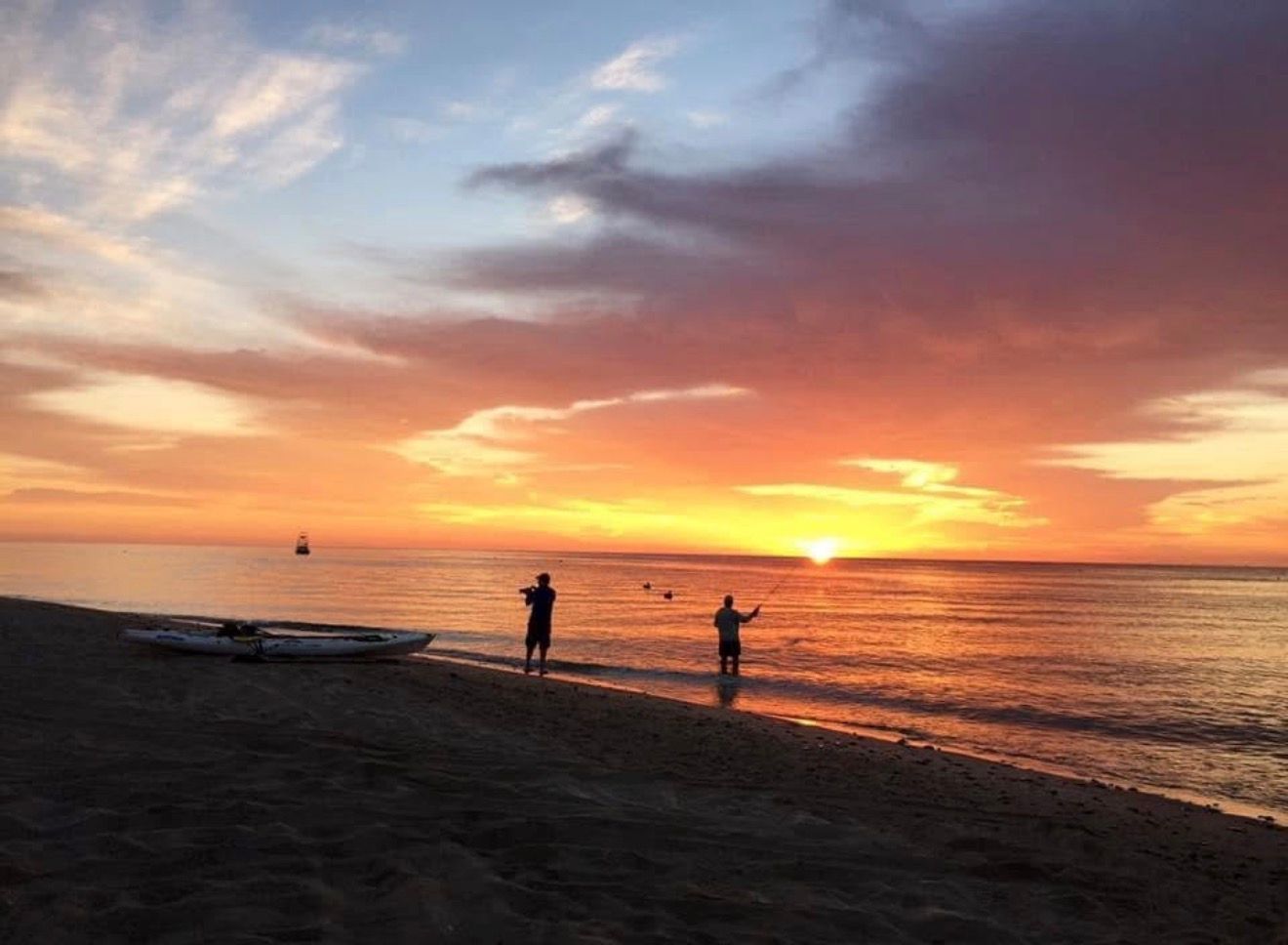 Sunset over calm ocean with two people standing on a beach silhouette