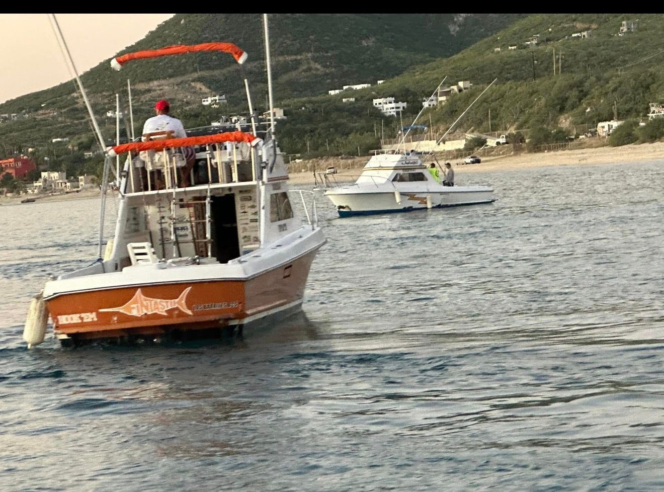 Two boats on choppy water near a rocky shoreline, one orange-and-white boat in the foreground.