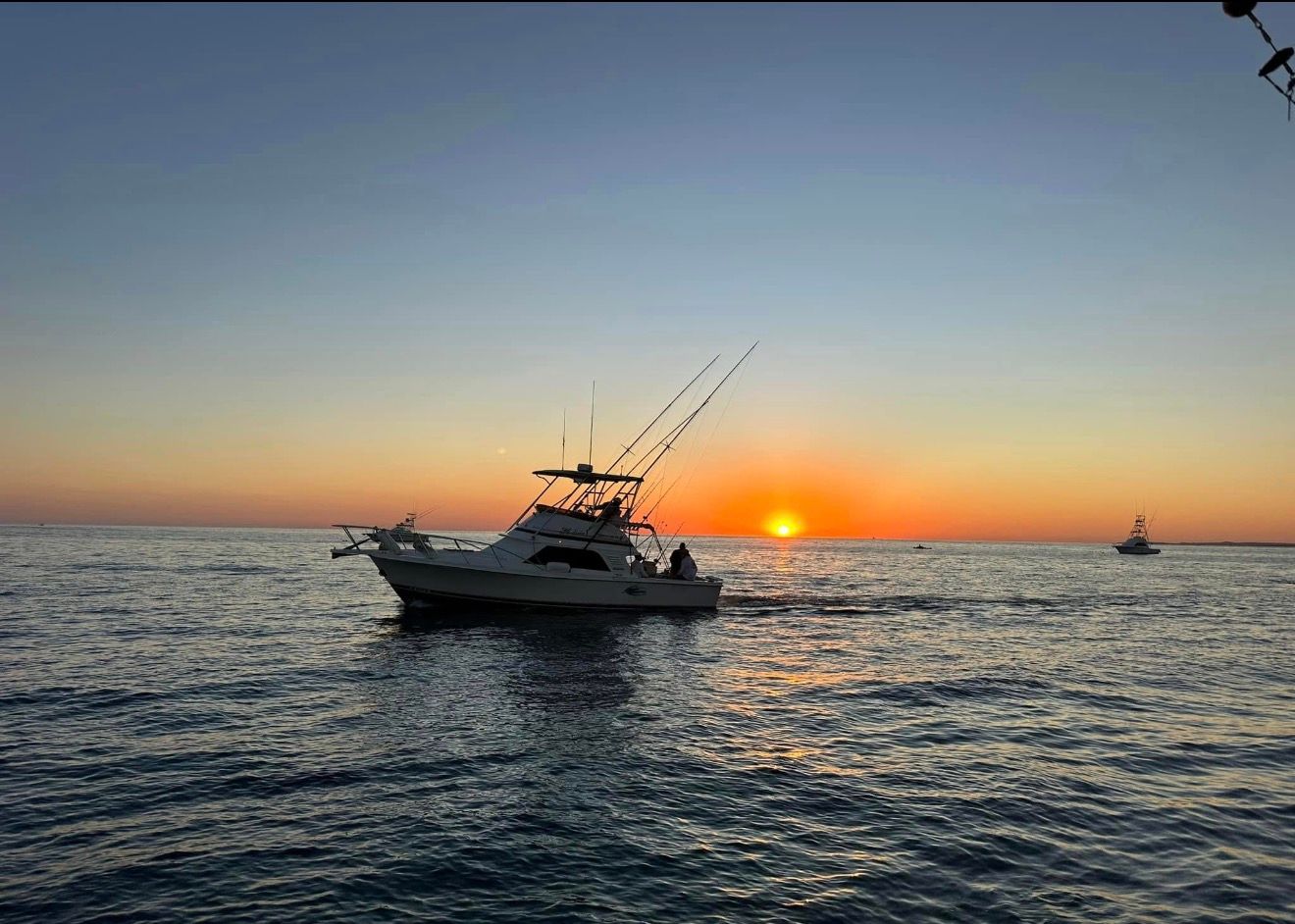 Boat silhouetted on calm sea at sunset with orange horizon and a distant sailboat.