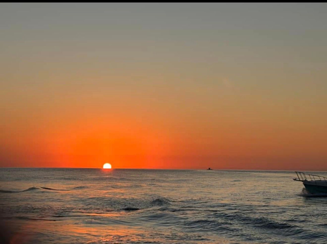Sunset over calm ocean with orange sky and a boat on the right