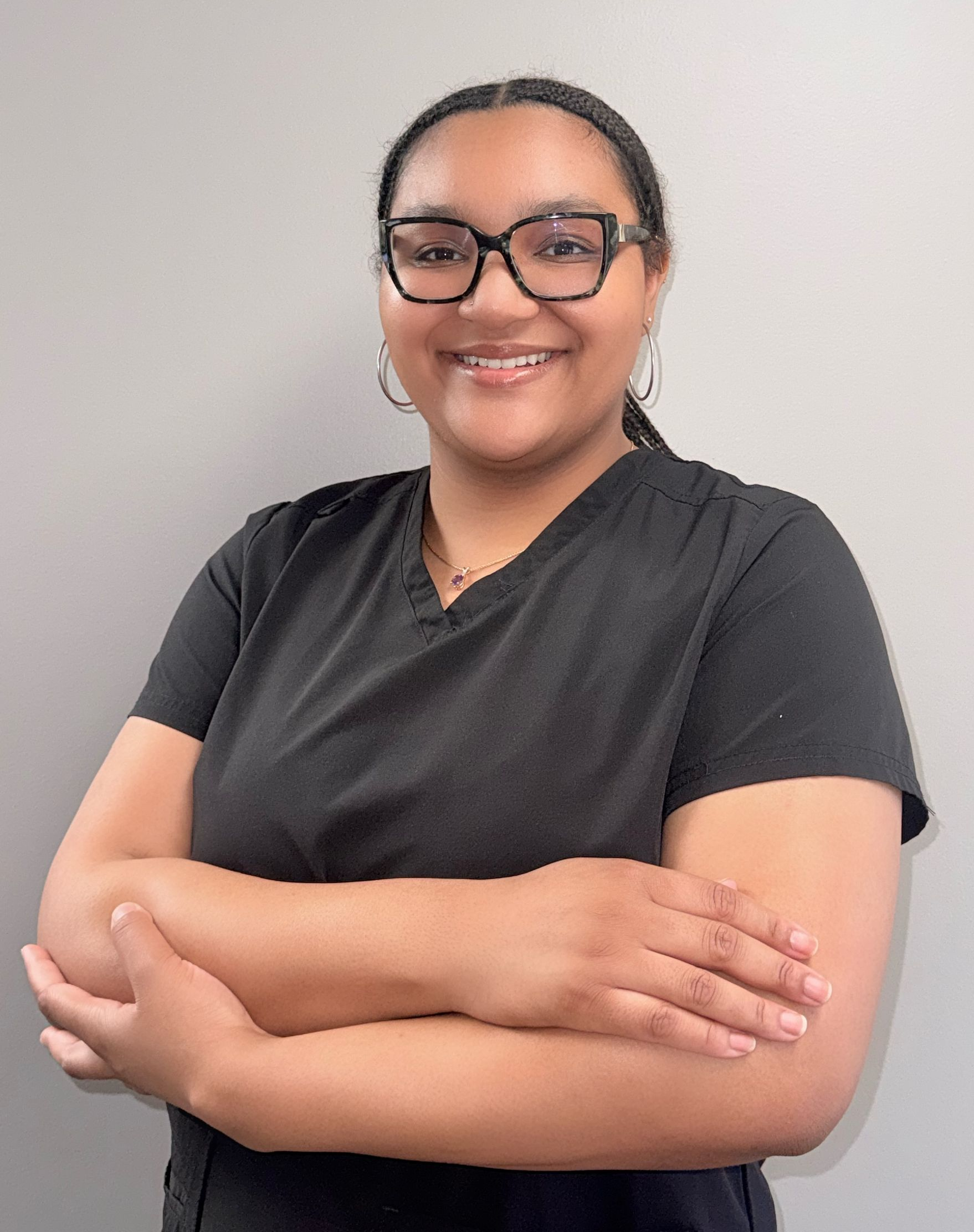 A woman wearing a black scrub top and a necklace is smiling for the camera.