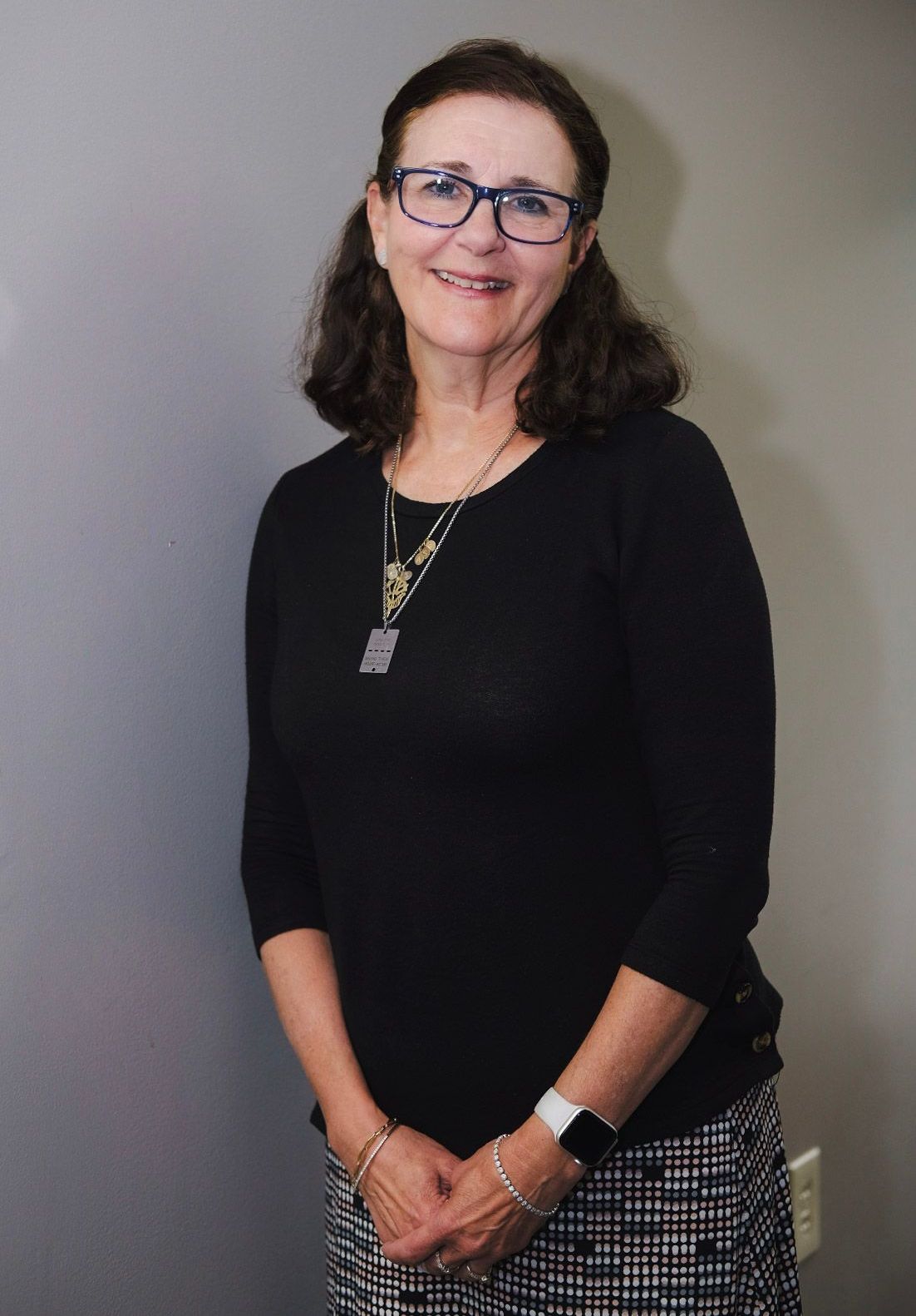 A woman wearing a black sweater and a necklace is smiling for the camera.