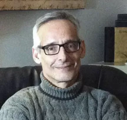A man wearing glasses and a sweater is sitting in a chair.