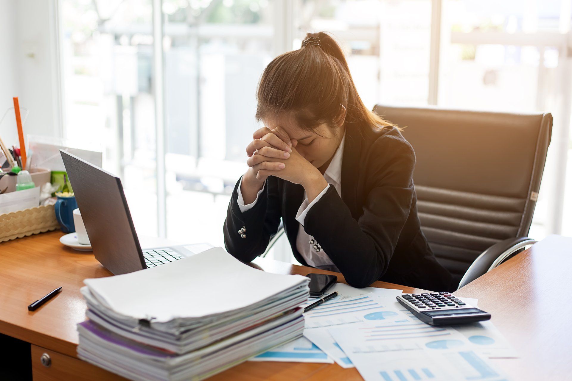 A woman is sitting at a desk with her head in her hands.