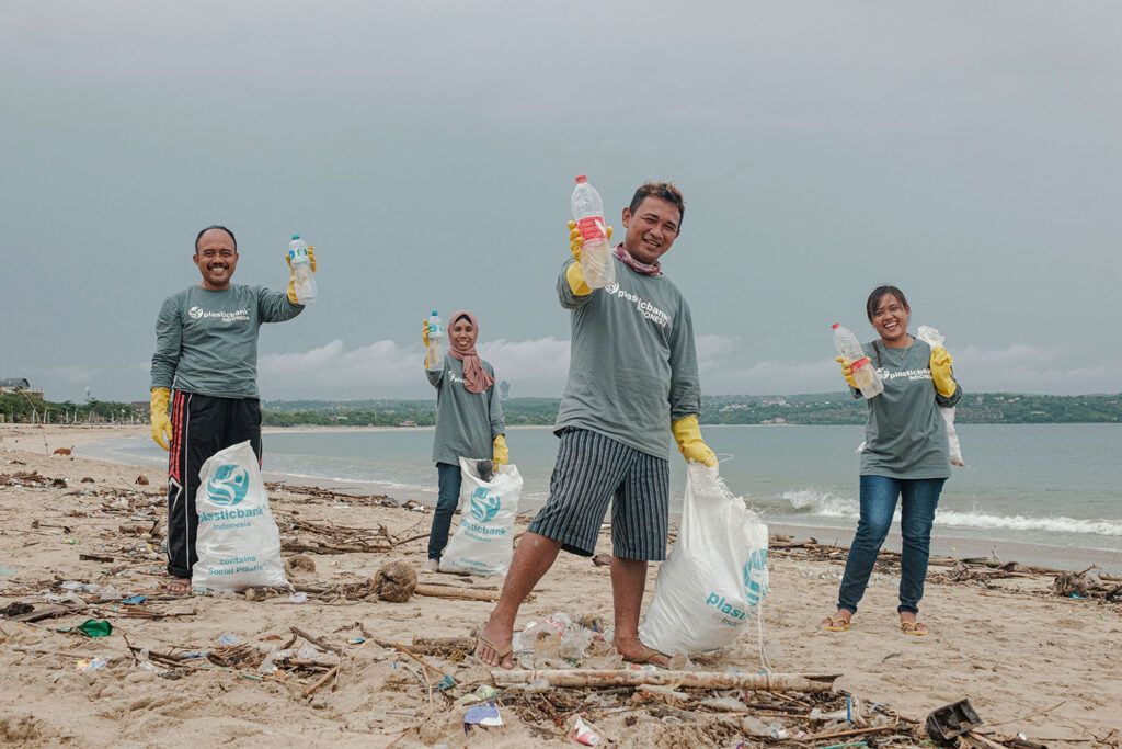 Volunteers on a beach hold trash bags and collected plastic litter during a cleanup drive