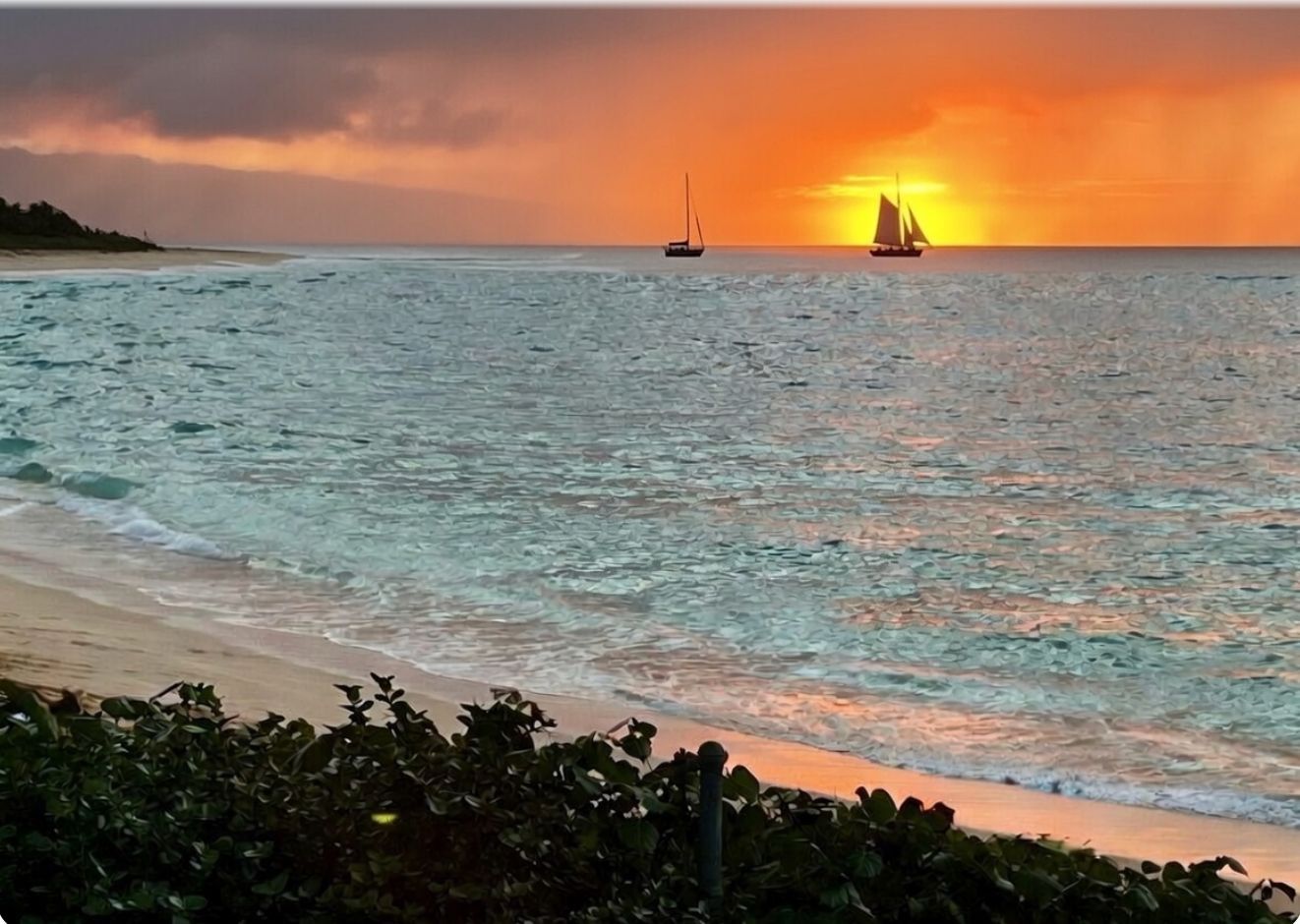 Sunset over a calm beach with sailboats silhouetted on the horizon