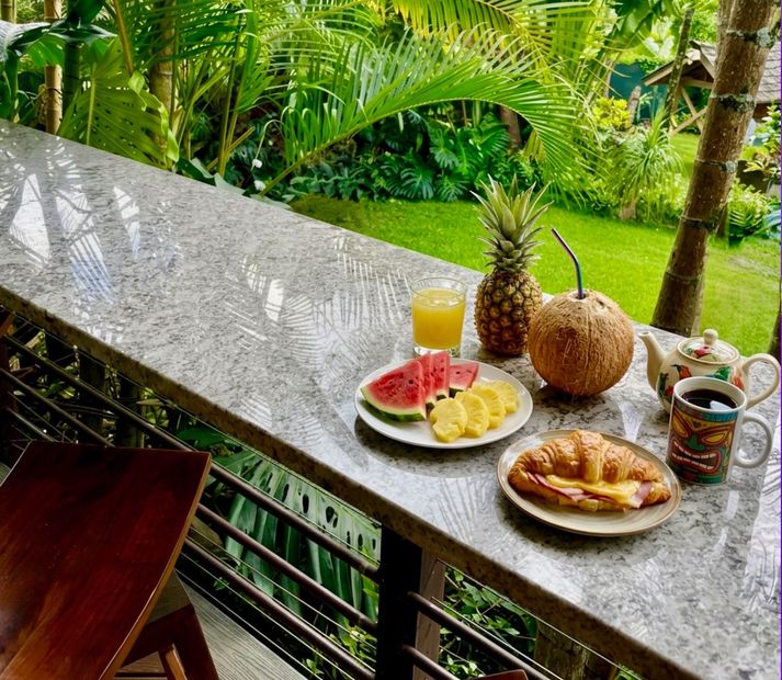 Breakfast spread on a balcony with fruit, juice, coffee, and pastries overlooking lush green garden views Breakfast spread on a balcony with fruit, juice, coffee, and pastries overlooking lush green garden views