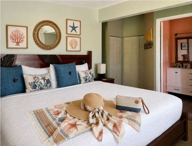Bedroom with red bed runner, patterned pillows, wall art, and open closet and bathroom doors Bedroom with red bed runner, patterned pillows, wall art, and open closet and bathroom doors