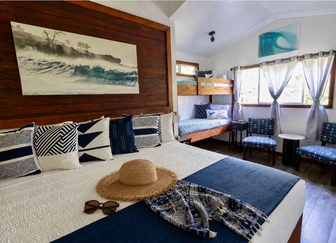 A rustic bedroom with two beds, each draped in white mosquito netting, with a lamp between them and a small window. A rustic bedroom with two beds, each draped in white mosquito netting, with a lamp between them and a small window.