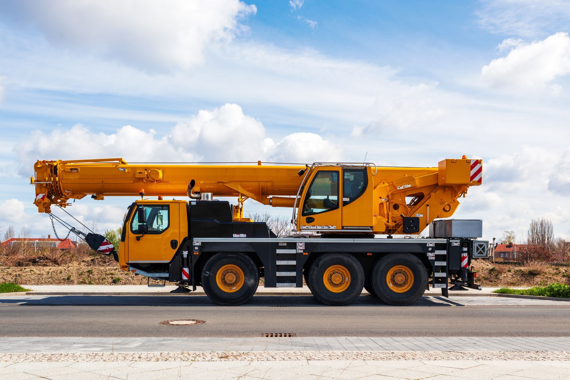 Yellow mobile telescopic crane with extended boom parked on a paved surface