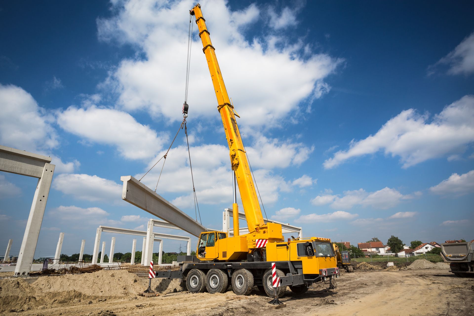 Yellow mobile crane lifting a large concrete beam at an active construction site. Yellow mobile crane lifting a large concrete beam at an active construction site.