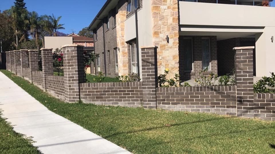 A house with a brick wall and a sidewalk in front of it.