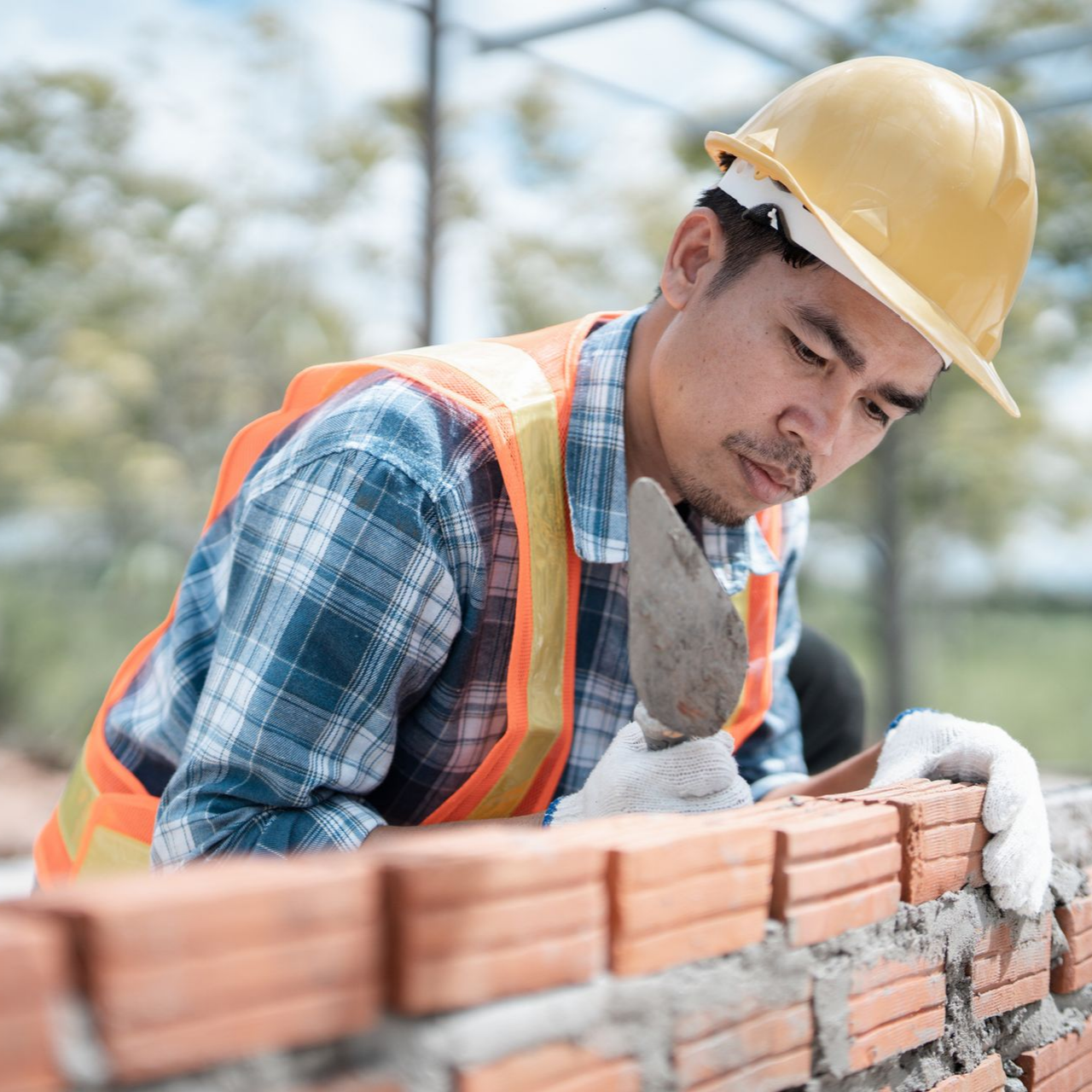 Construction worker performing commercial bricklaying on site wearing safety helmet and vest. Construction worker performing commercial bricklaying on site wearing safety helmet and vest.