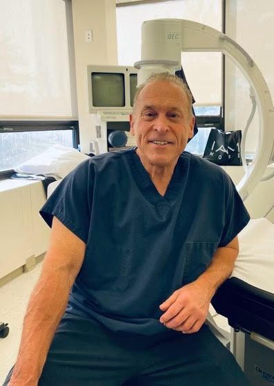A man in a scrub is sitting on a bed in a hospital room.