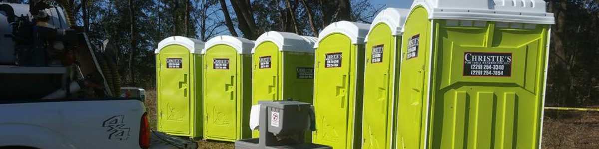 A row of bright lime-green portable toilets lined up outdoors next to a parked truck.