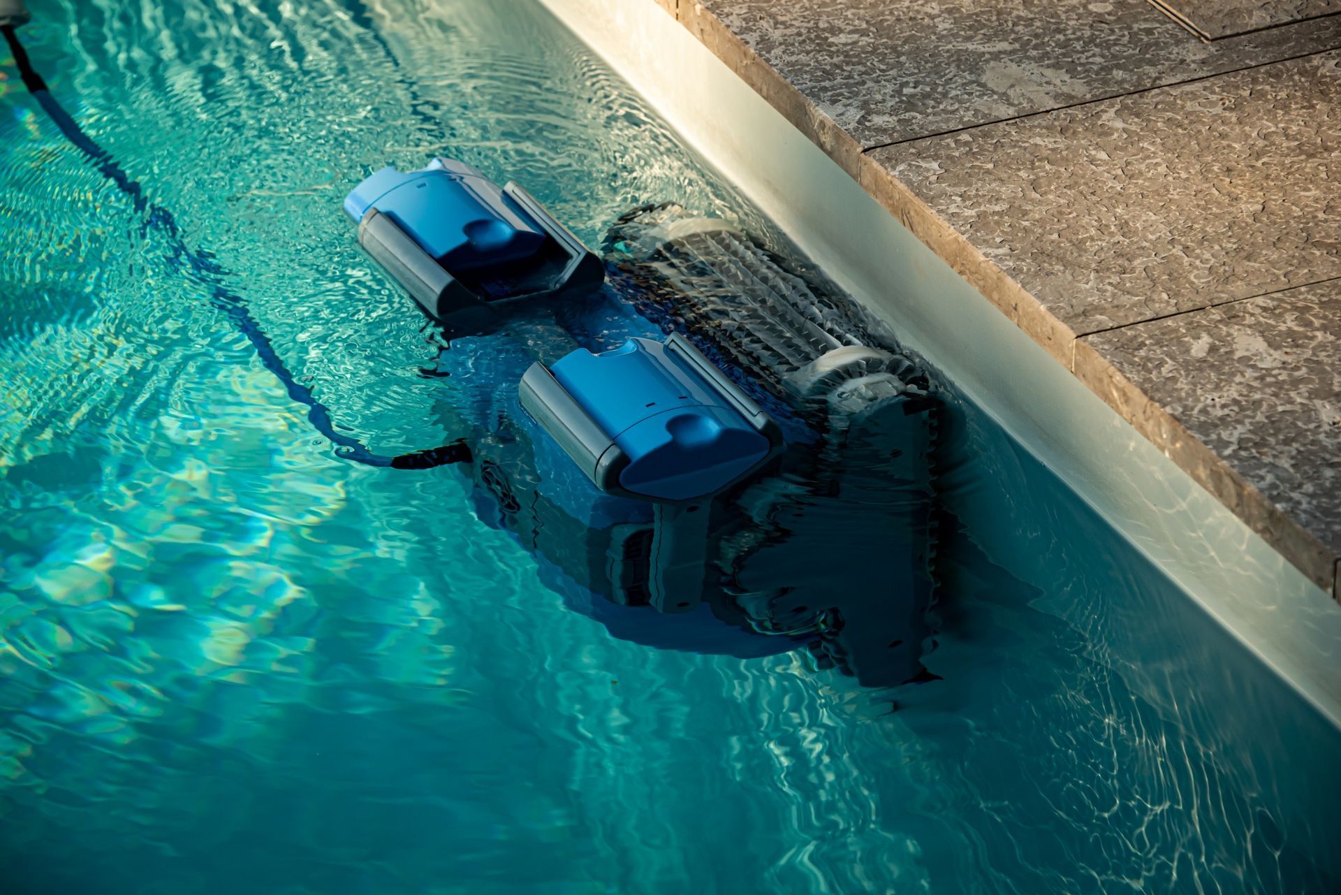 A blue robotic pool cleaner climbs the wall of a swimming pool.