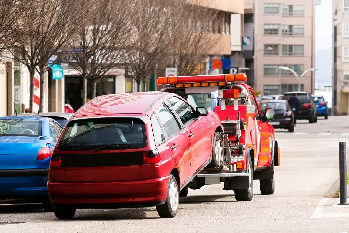 Red car being towed by a tow truck on a city street.