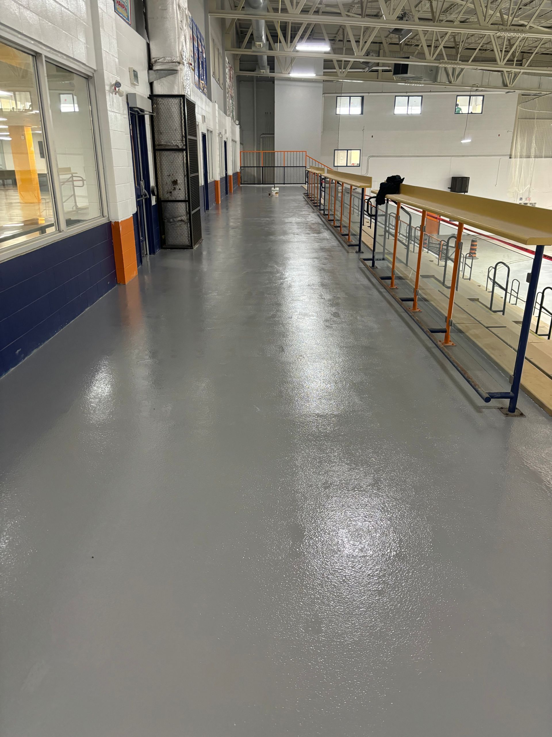 A long hallway in a building with a gray floor and a railing.