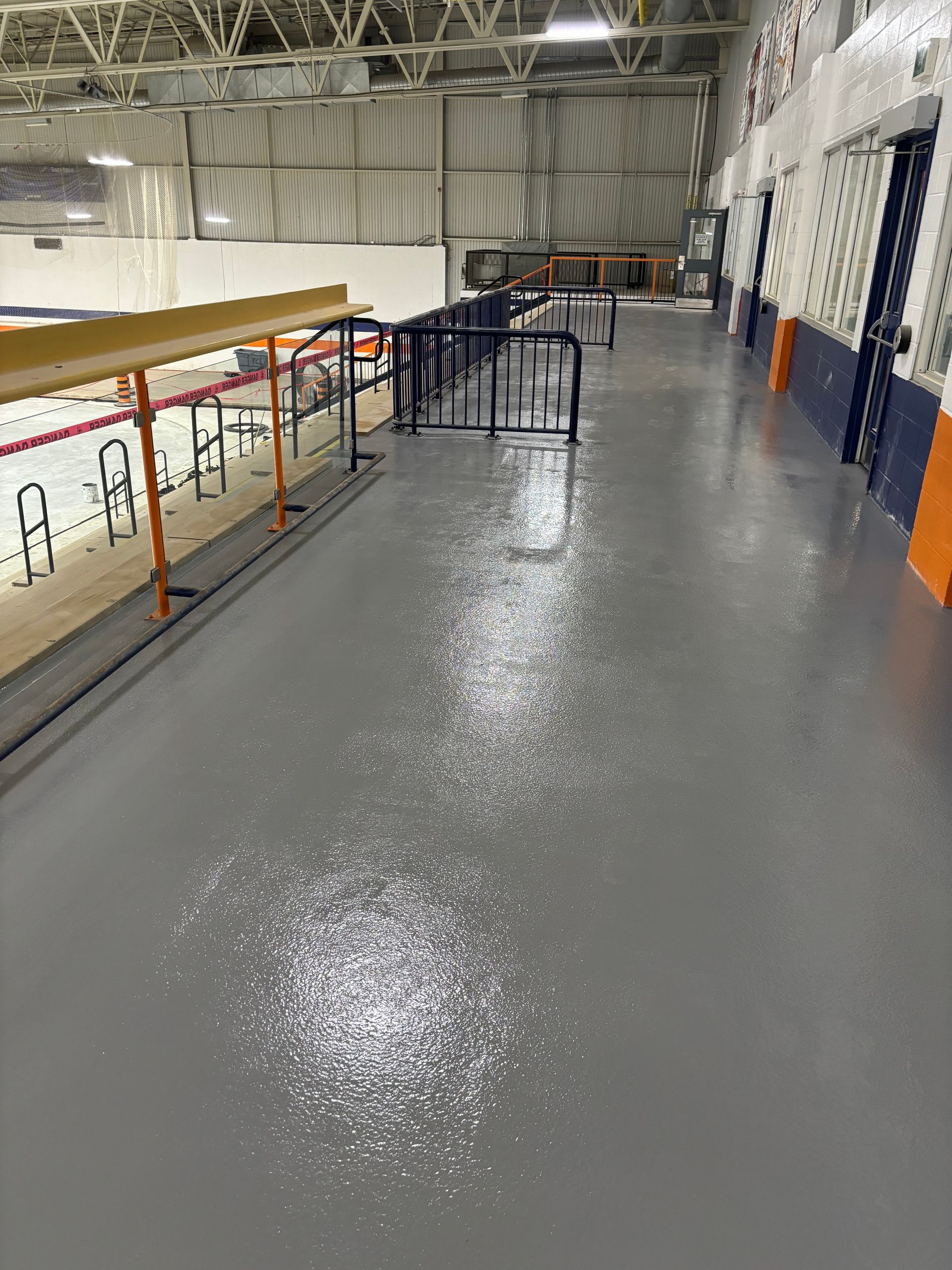 A long hallway in a building with a gray floor and a railing.