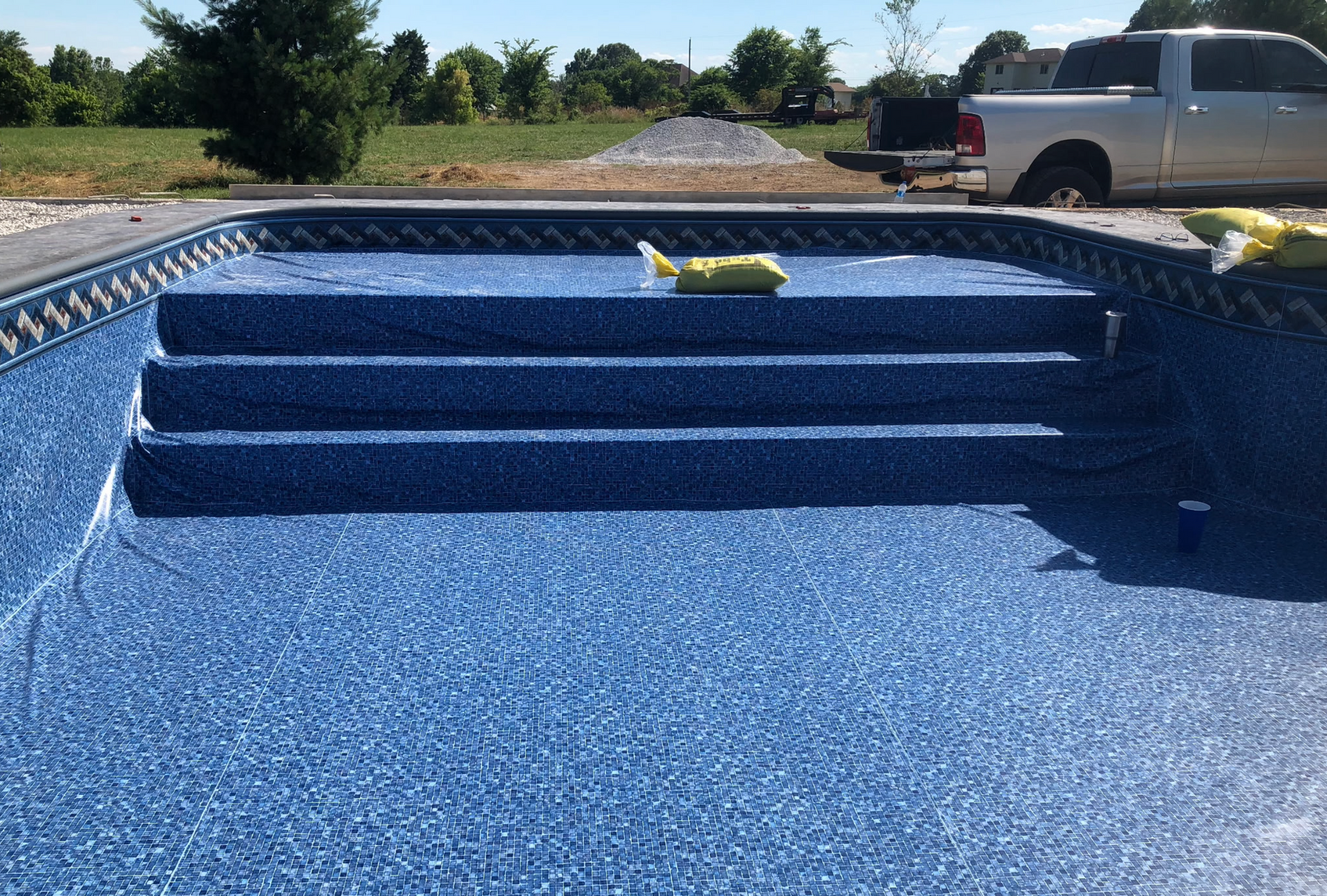 Empty blue-lined swimming pool under construction with steps and a pickup truck in the background