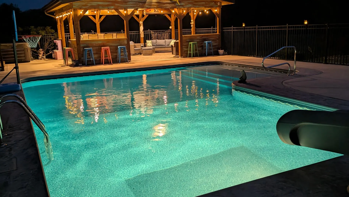 Lit swimming pool at night with a lit gazebo and patio beside it