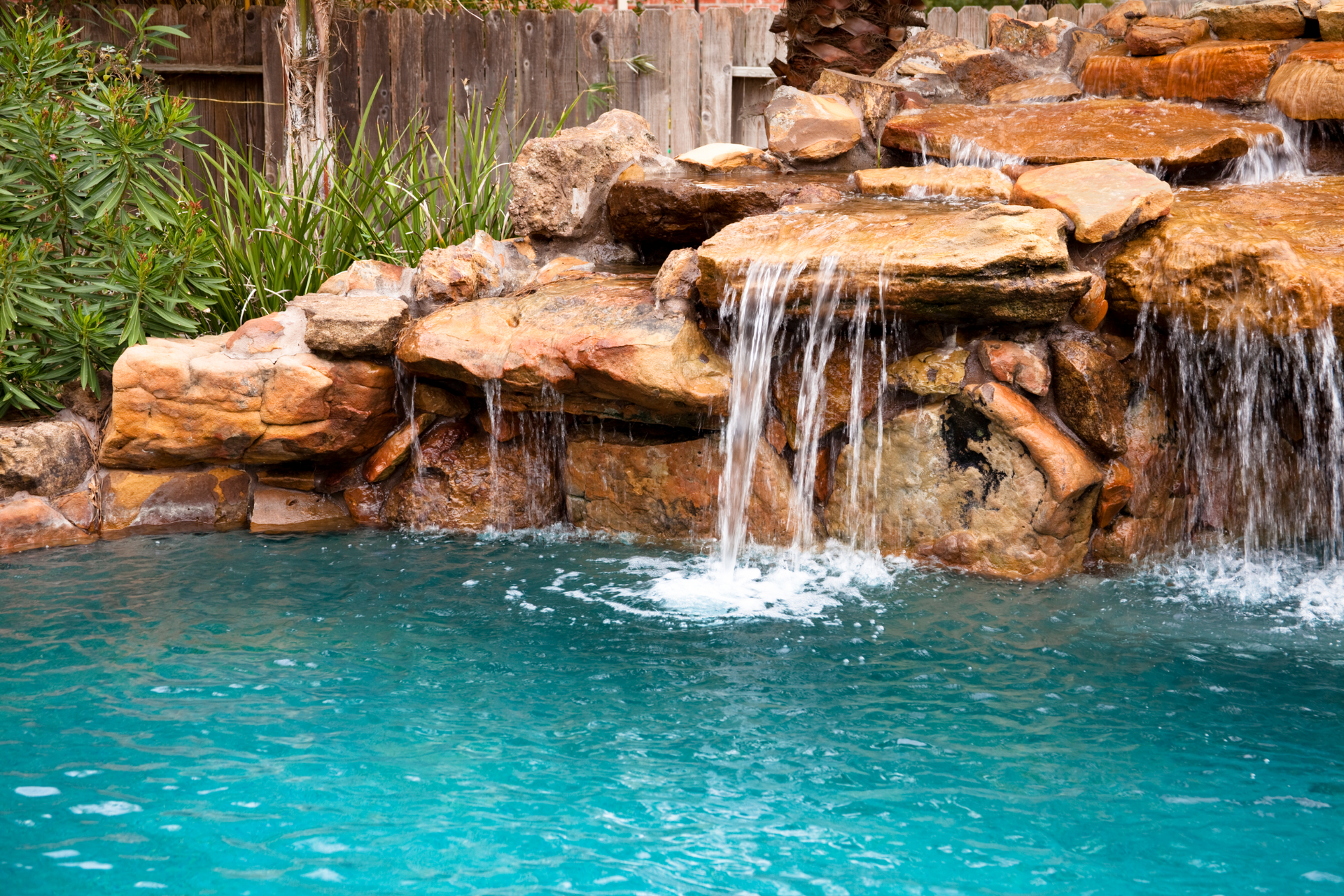 Rock waterfall spilling into a turquoise pool beside stacked brown stones and greenery