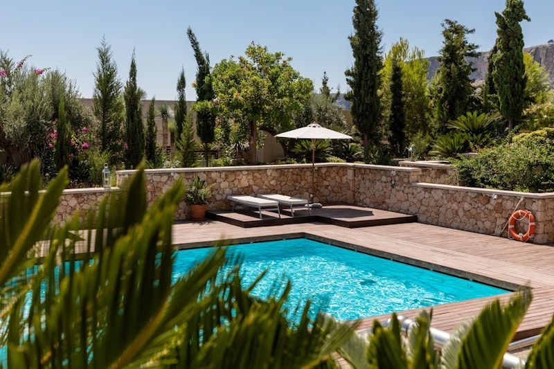 Backyard swimming pool with stone deck, lounge chairs, and lush green garden plants