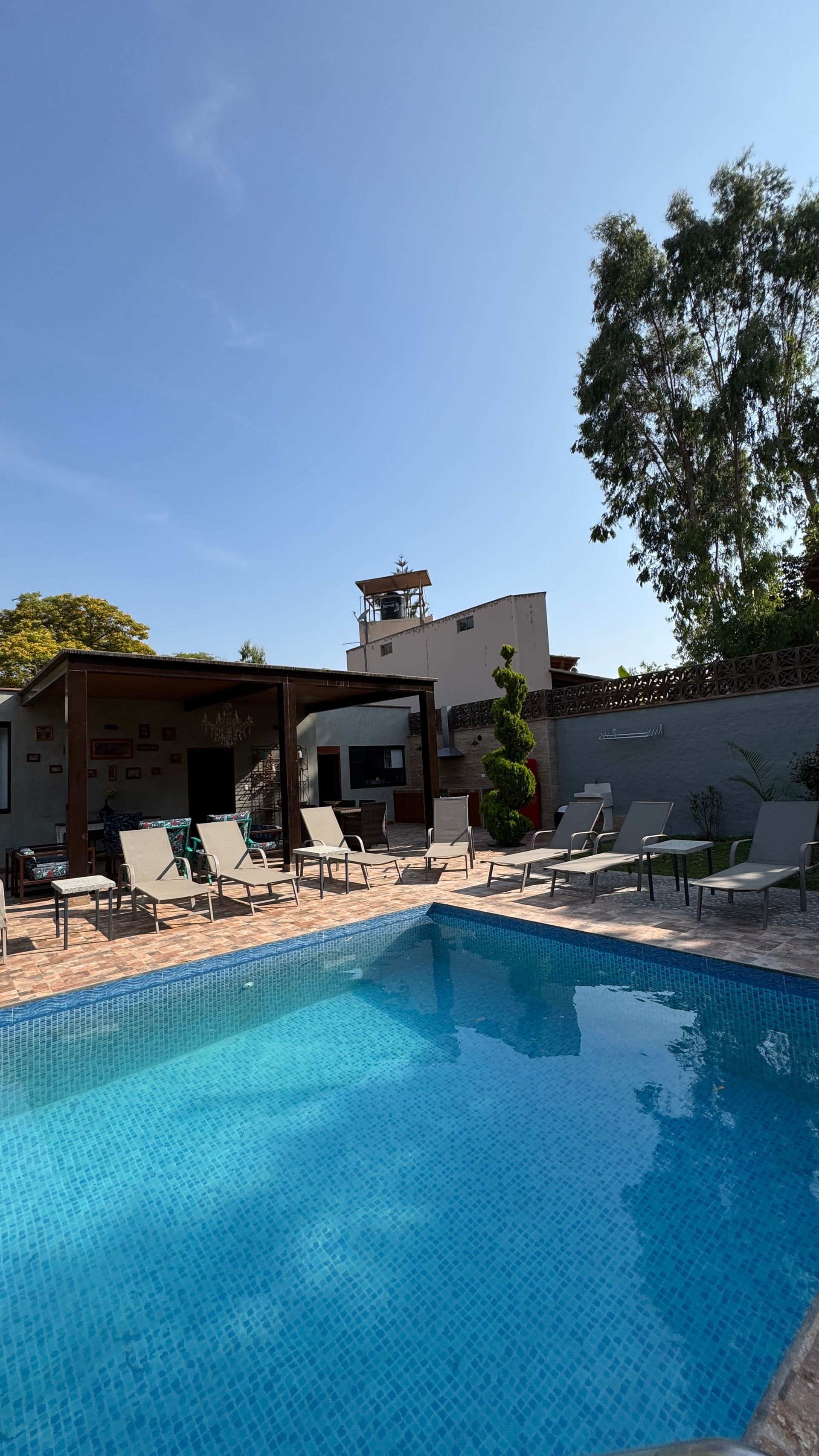 Swimming pool with lounge chairs, building in background, blue sky.