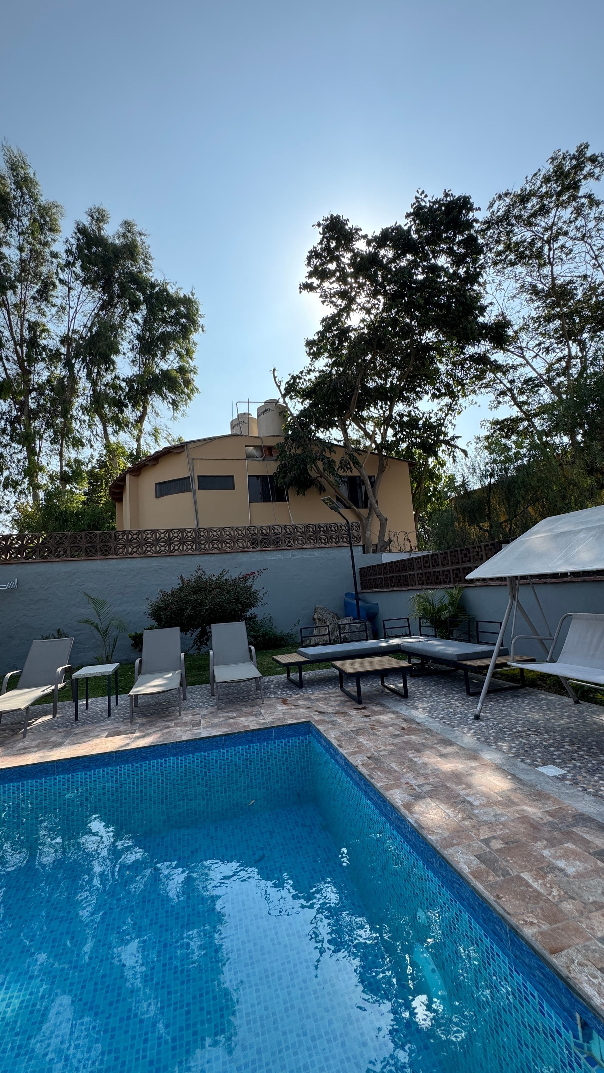 Swimming pool with lounge chairs, building, and trees on a sunny day.