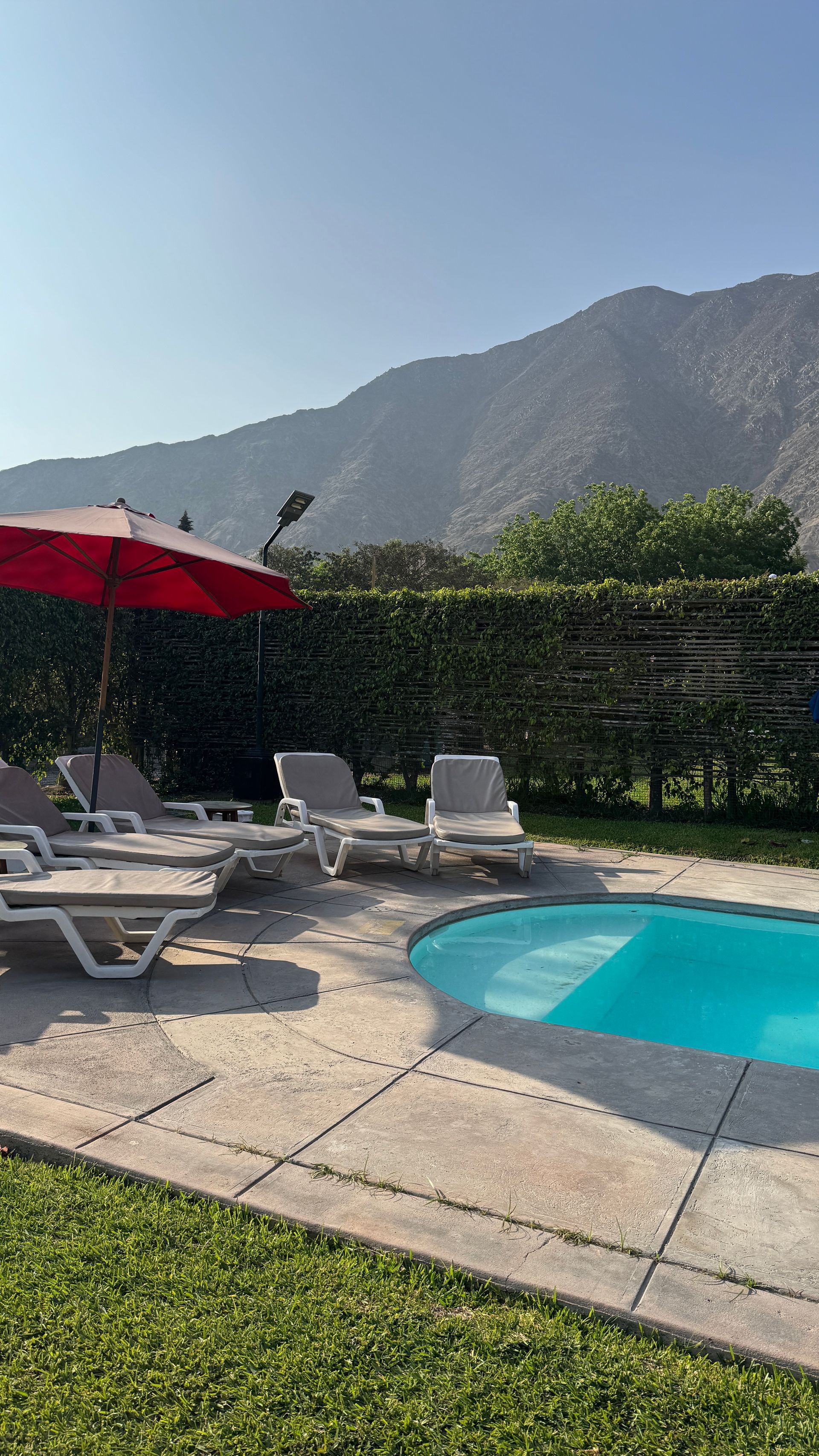 Poolside scene with lounge chairs, red umbrella, and mountain backdrop.