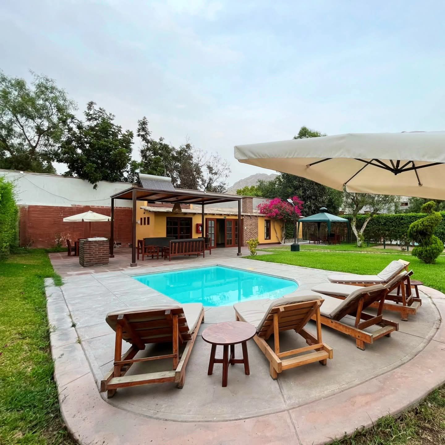 Swimming pool surrounded by lounge chairs, patio, and small buildings; cloudy day.