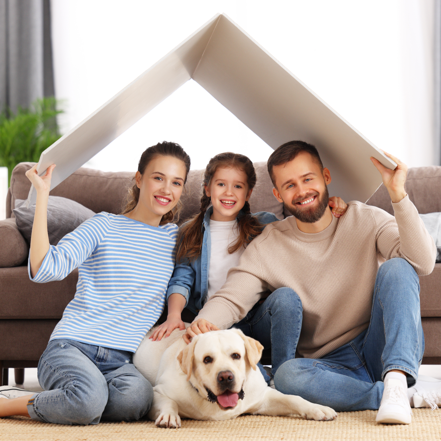 Three people sitting with a dog in a cozy living room, smiling under a blanket fort