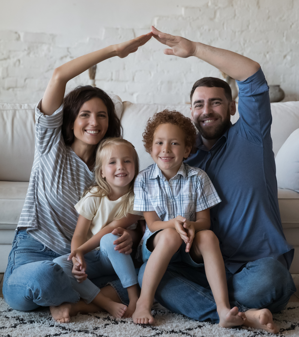 Family of four sitting on a couch, smiling and making a heart shape with their arms