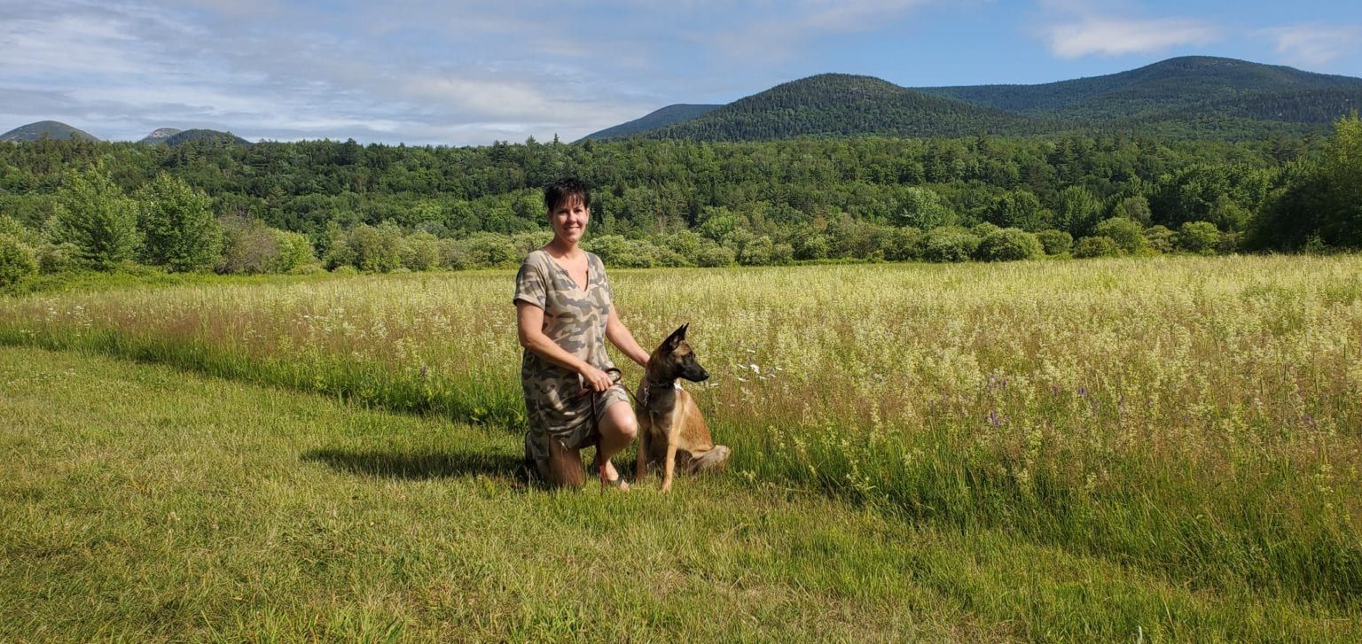A woman is kneeling down next to a dog in a field.