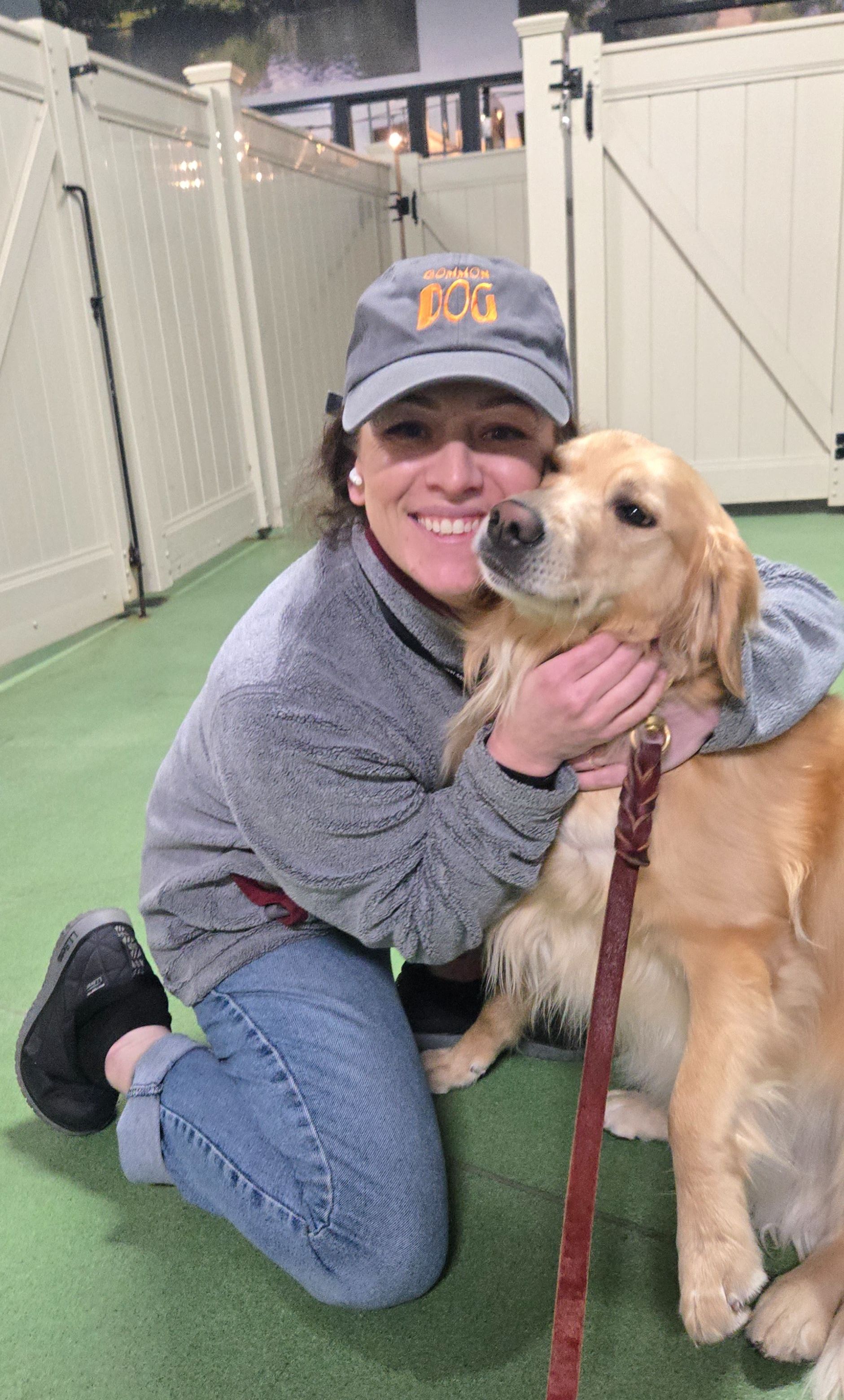 A woman is kneeling down next to a dog on a leash.