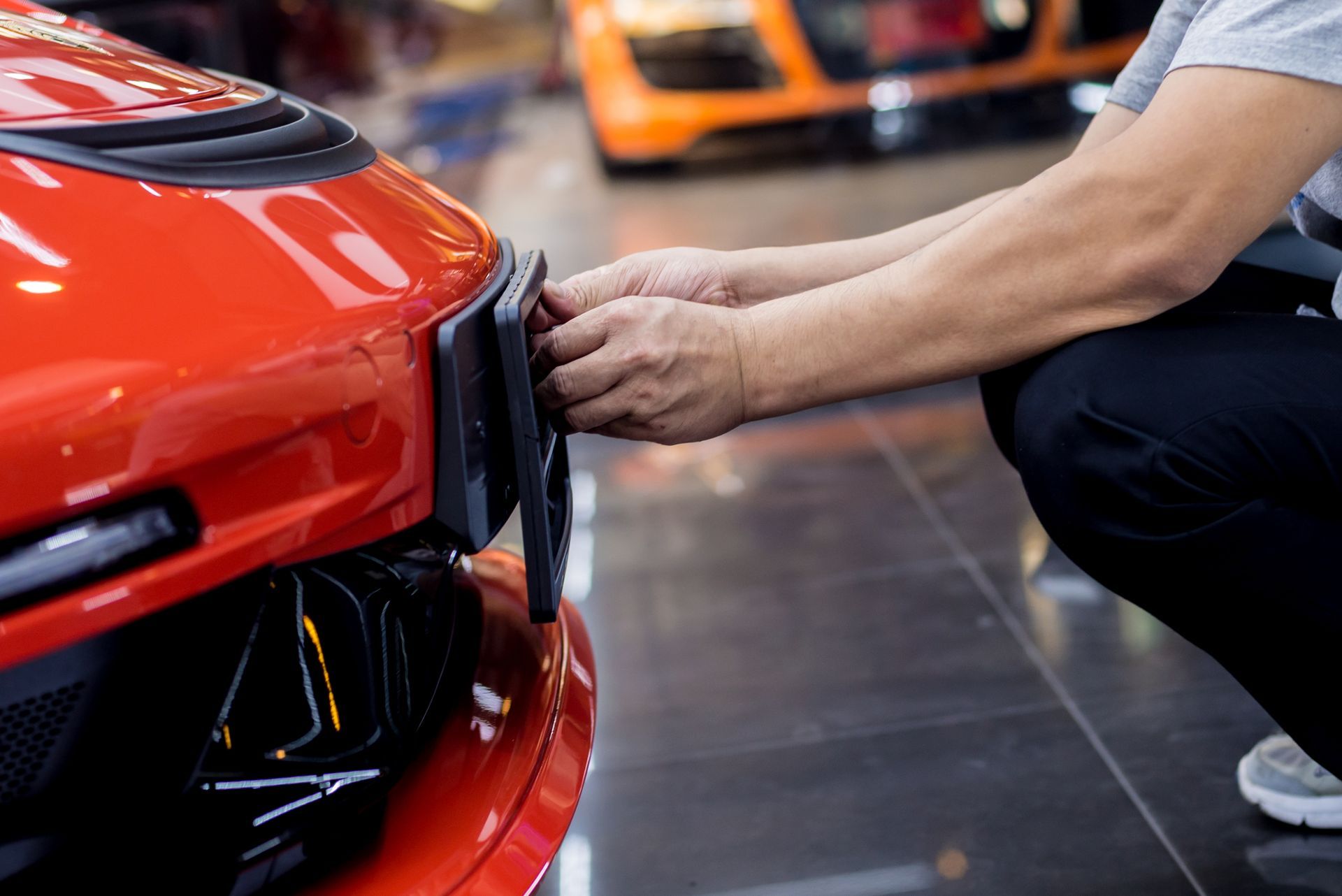 Person adjusting a red sports car's front bumper in a garage