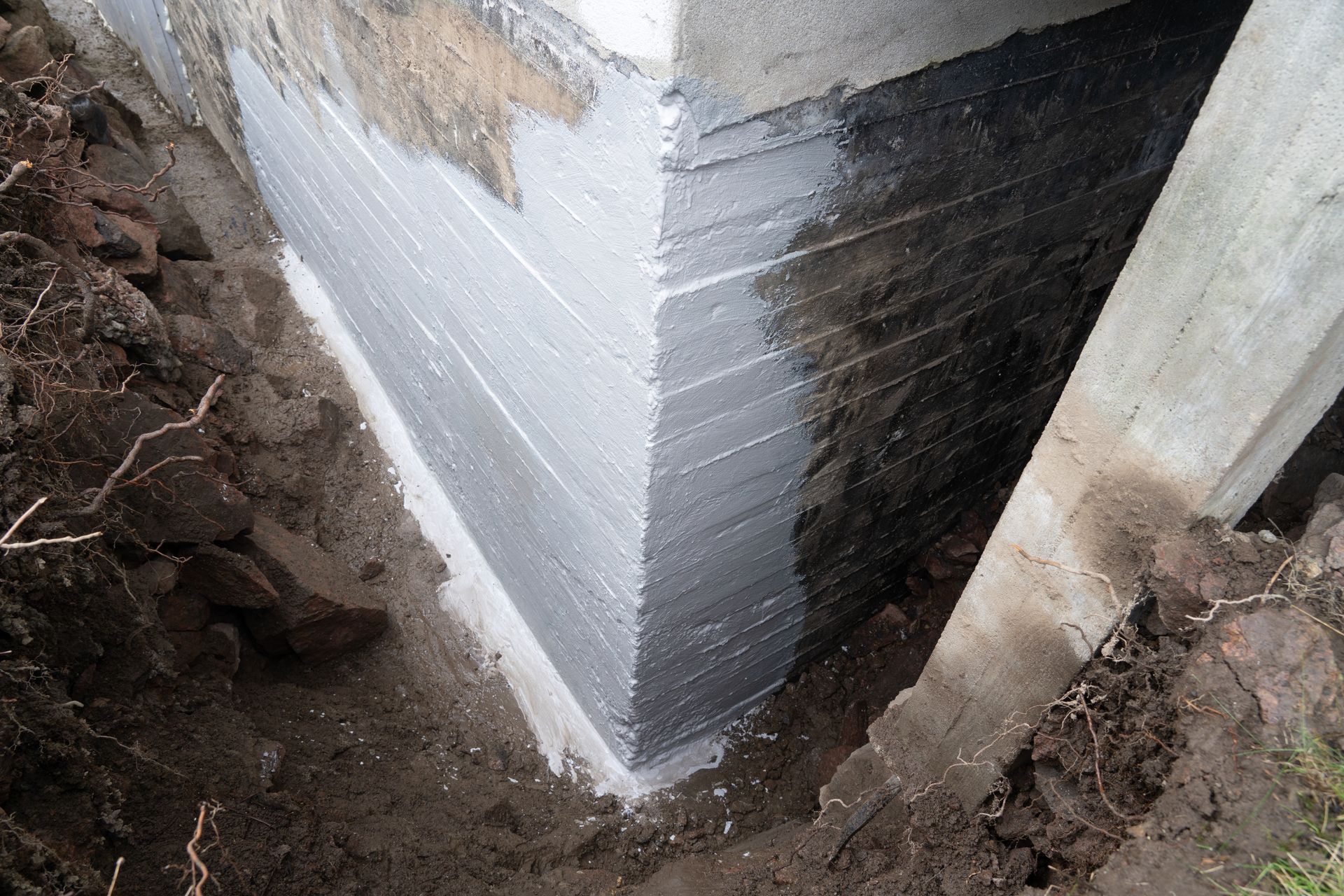 Corner of a building foundation with white waterproof coating and exposed soil around it