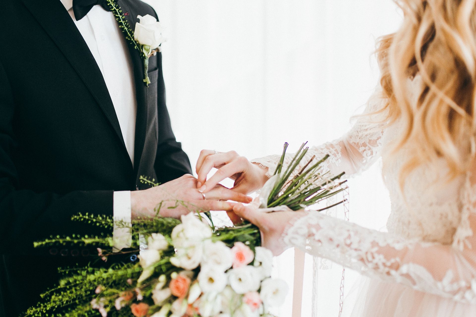 Bride and groom exchanging rings during a wedding ceremony, with bouquet and white floral details