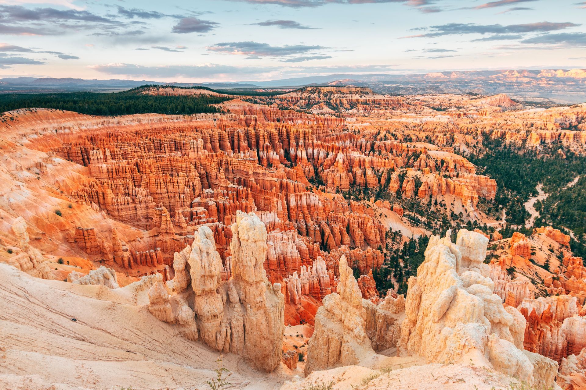 Orange hoodoos and cliffs in a vast canyon under a partly cloudy sky