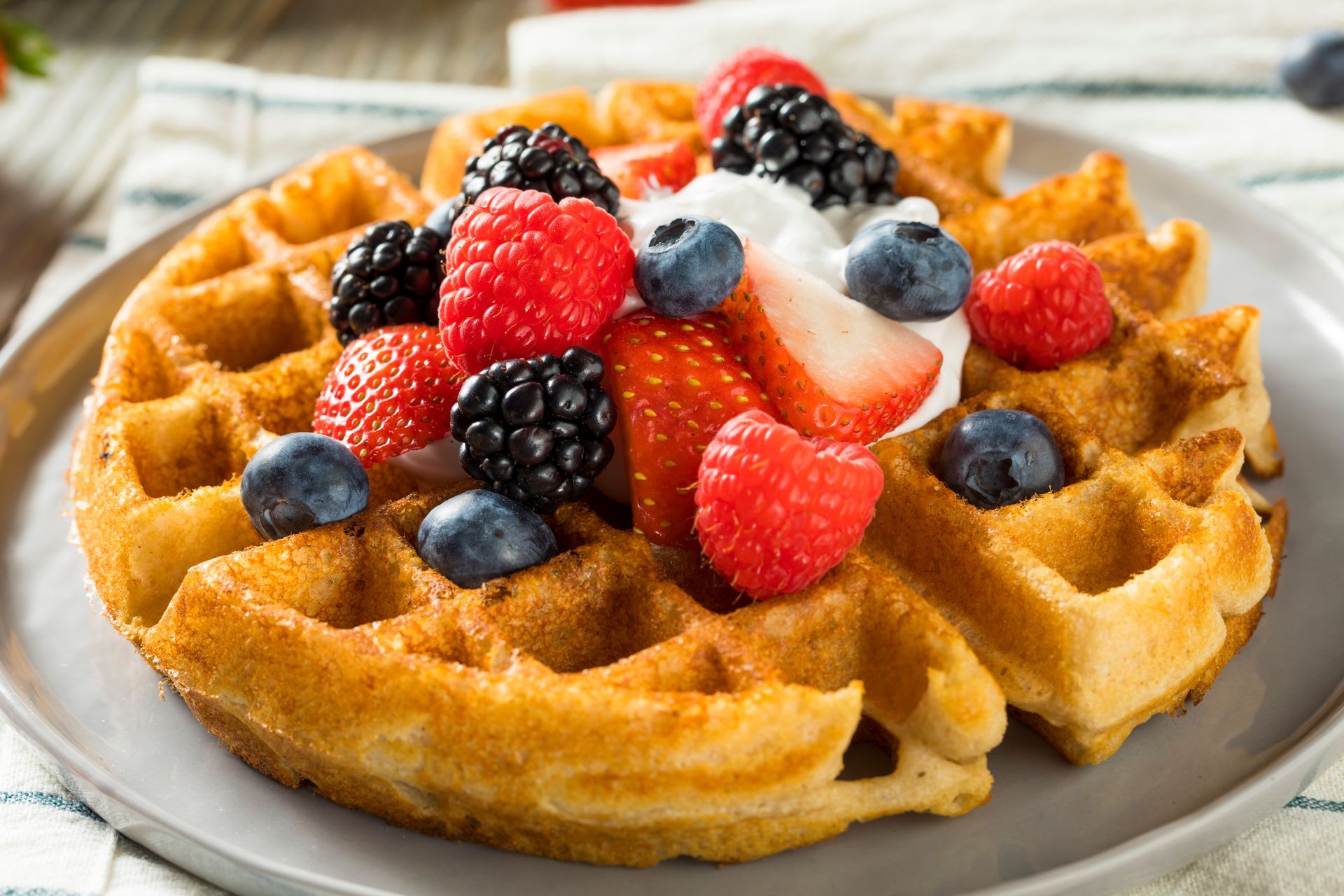 Waffle topped with strawberries, blueberries, blackberries, and cream on a white plate