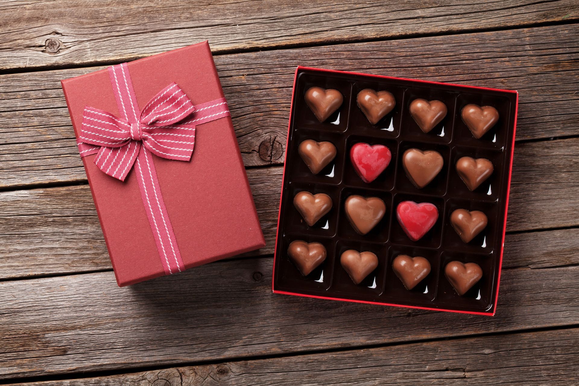 Open pink gift box beside a red chocolate heart assortment on rustic wood background
