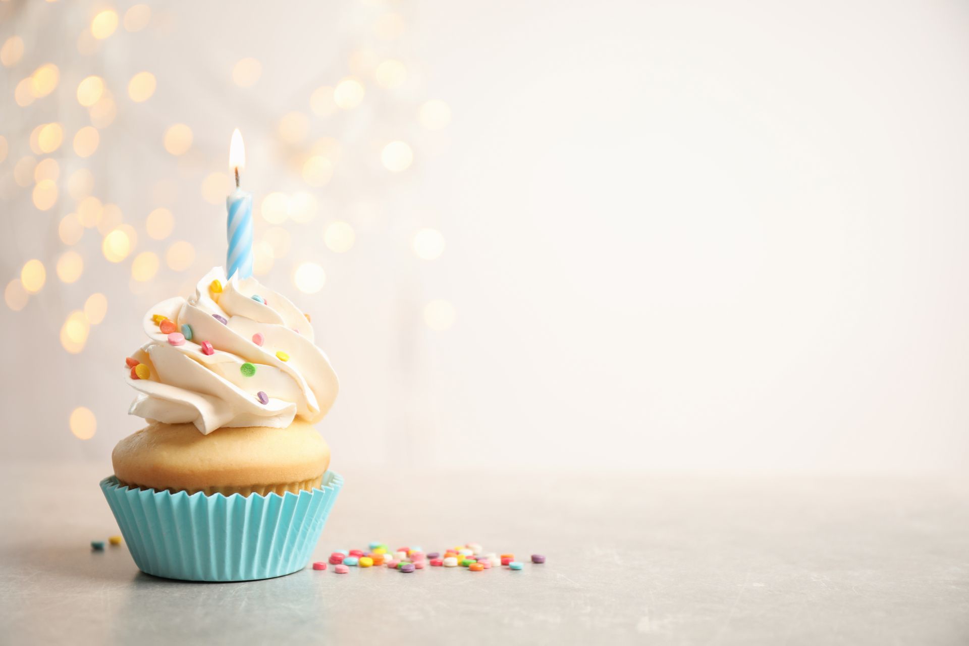 Cupcake with white frosting, sprinkles, and a blue candle in a blue wrapper on a gray surface