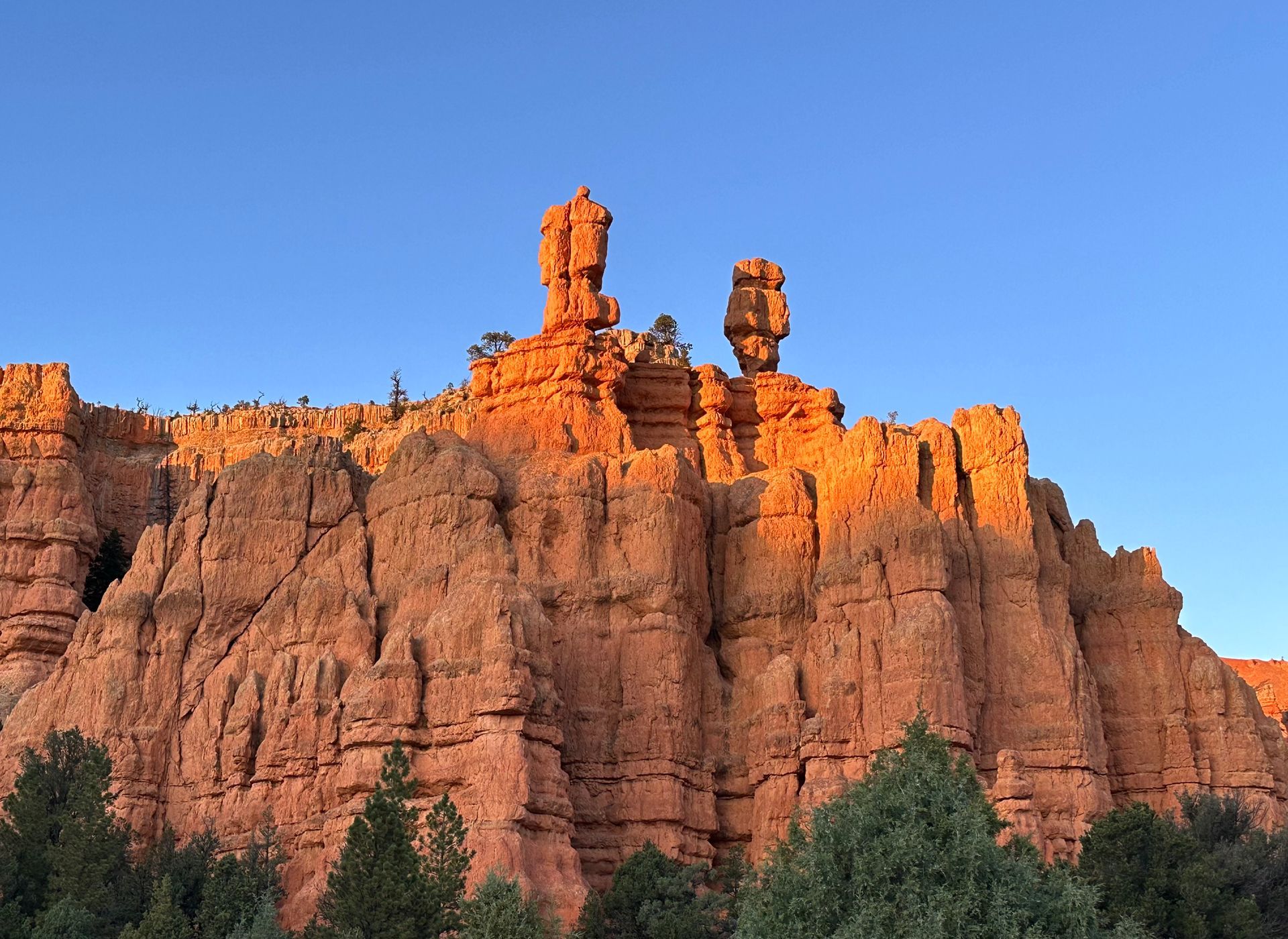 Sunlit orange and white hoodoos in a Bryce Canyon-like desert landscape under a cloudy sky