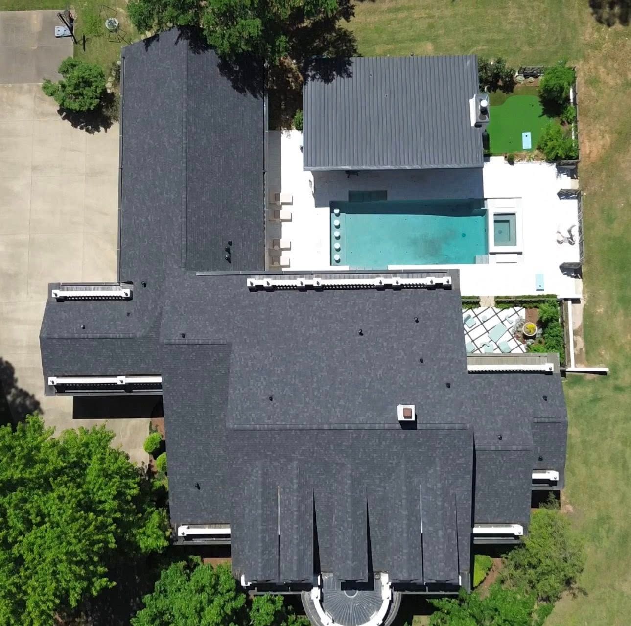 Overhead view of a modern house with a dark roof, a pool, and a grassy yard.