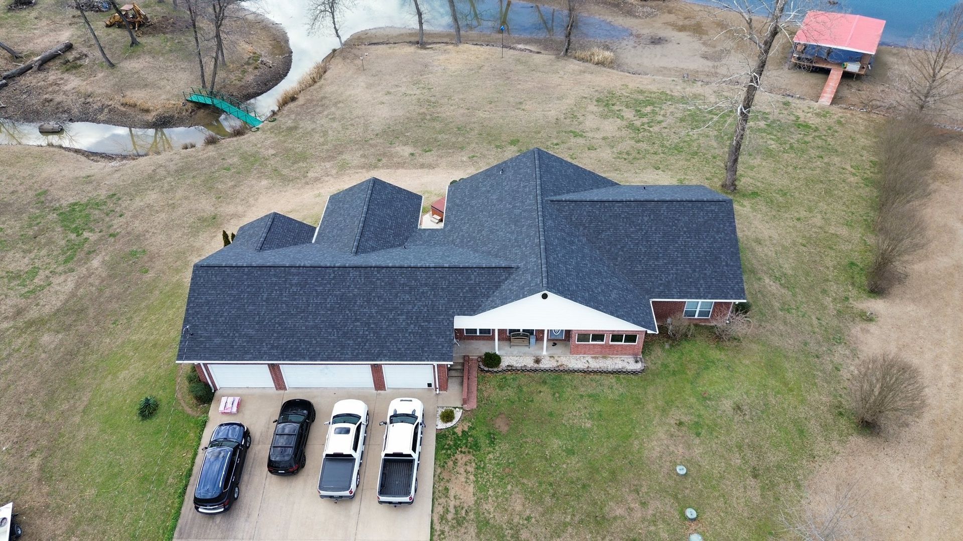 Aerial view of house with cars parked in the driveway, near a body of water.