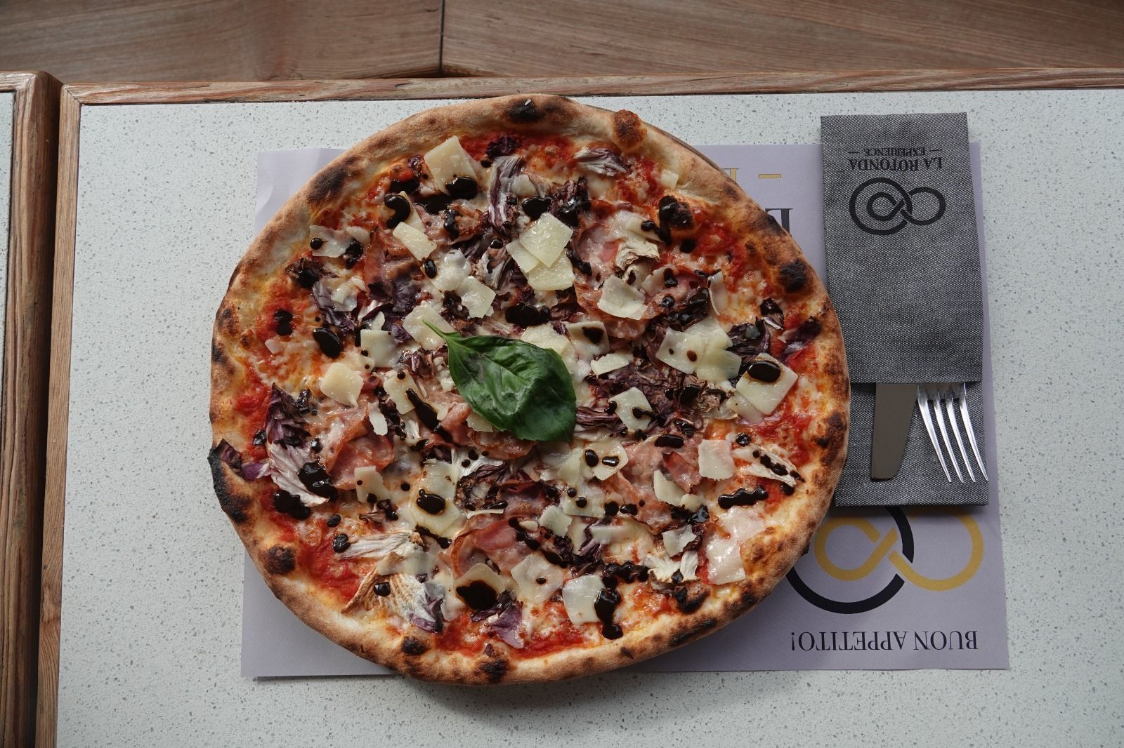 Pizza su una tovaglietta con forchetta e coltello su un tavolo di legno.