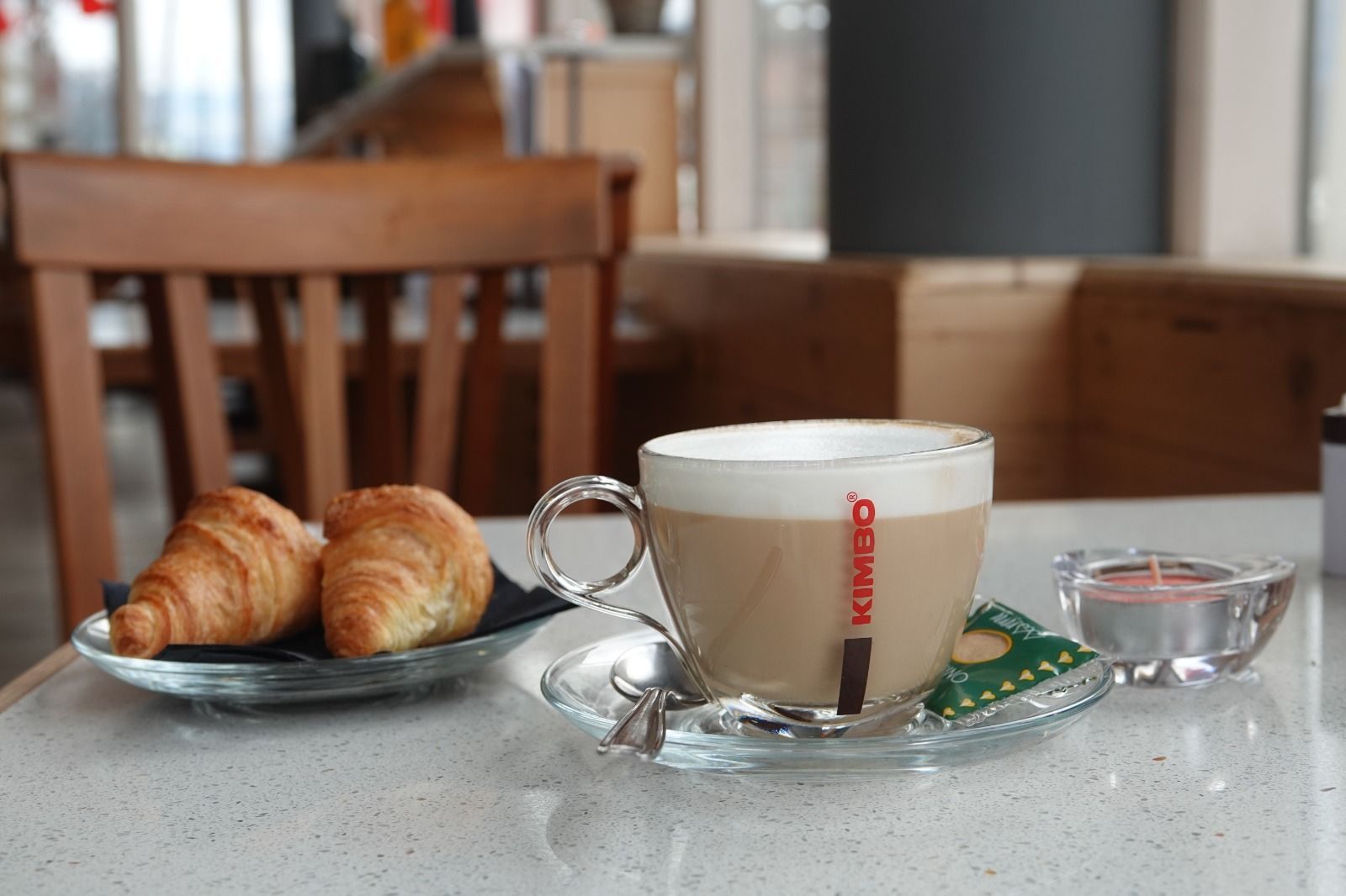 Una tazza di caffè nero su un piattino, appoggiata al tavolo di un bar, con uno sfondo sfocato di un ristorante.
